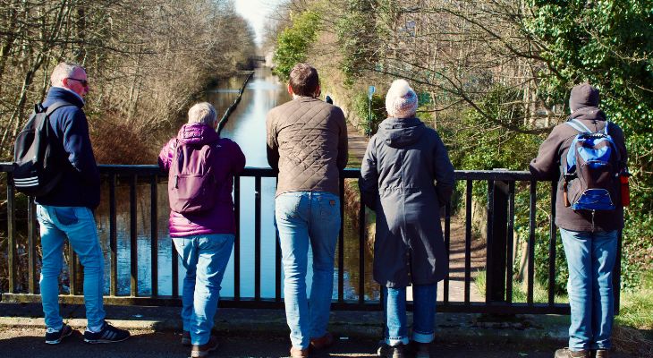 5 people stood on a bridge overlooking a canal.
