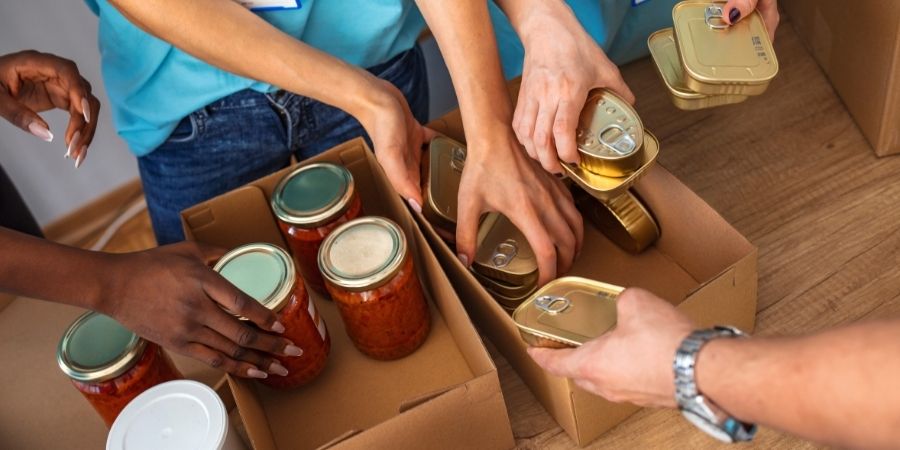 A group of people packing cans and jars of food into a box.