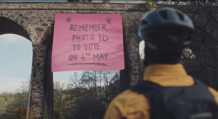 A man looking up at a sign underneath a bridge. The sign reads &quot;Remember photo ID to vote on fourth May&quot;