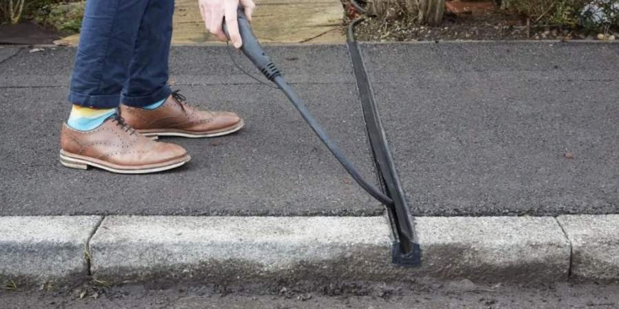 A person wearing blue pants and brown shoes places an electric cable in a covered channel that has been installed in the pavement.