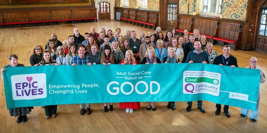 A large group of people stand behind a banner that reads Adult Social Care Rated as GOOD with a Care Quality Commission logo.