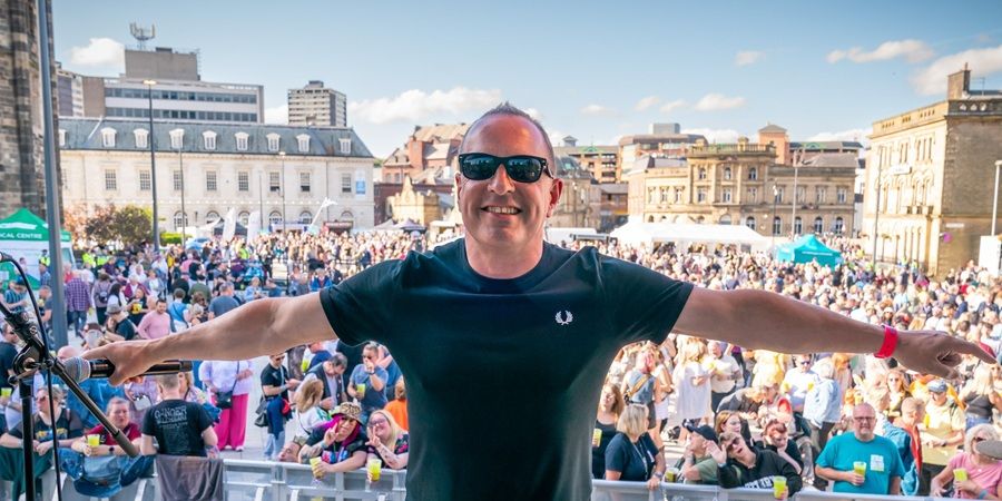 A person wearing sunglasses stands with their arms outstretched in front of a large crowd.