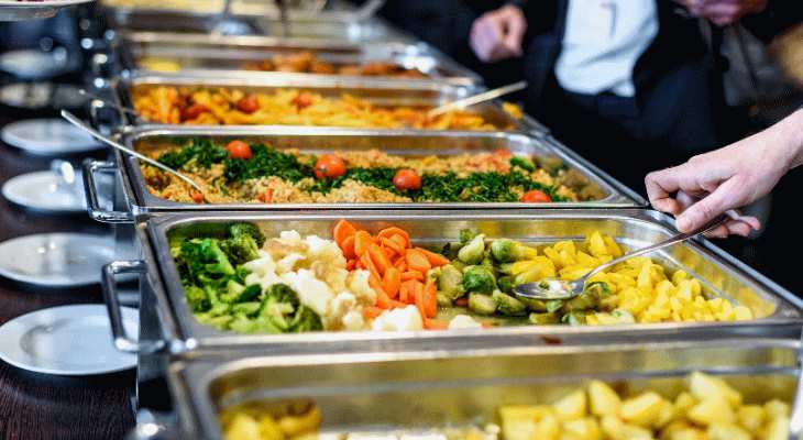 A buffet with hot food in silver serving trays.