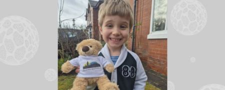 A smiling child holds a teddy bear wearing a white t-shirt with the words "Raising Rochdale" and a silhouette of buildings.