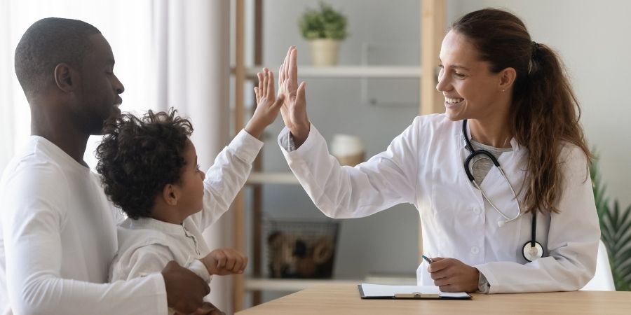 A health visitor high fiving a young child with their dad.