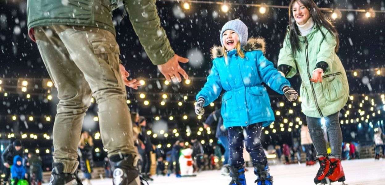 A child ice skating with 2 adults.