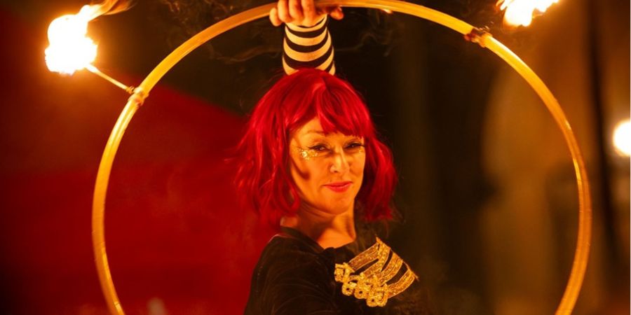 A performer holds a large, flaming hula hoop over their head