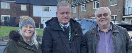 3 people stand in front of houses.