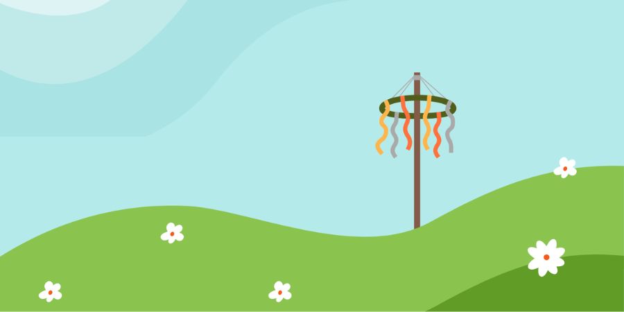 A maypole decorated with colorful ribbons stands on a green grassy hill dotted with white flowers under a light blue sky.