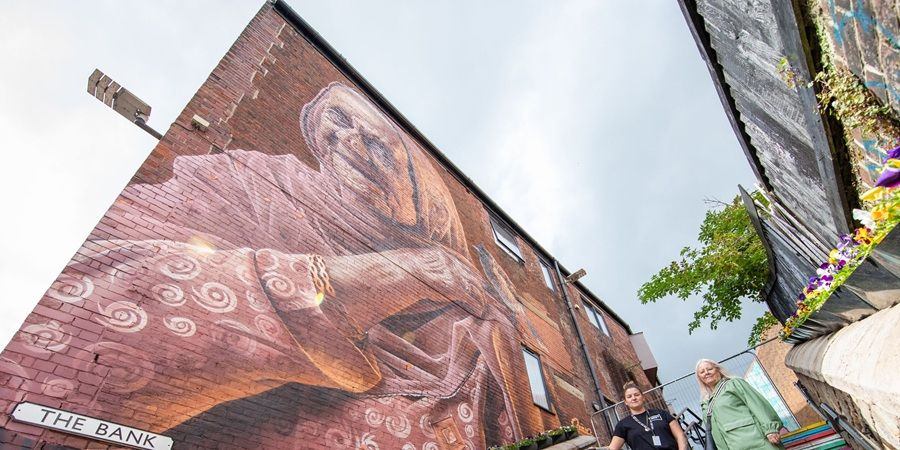 2 people walk past a mural on the side of a building.