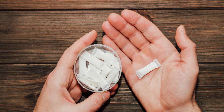 Hands holding a tin of nicotine pouches.