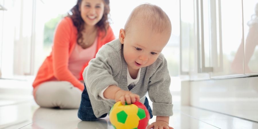 A mother watches her baby play with a ball.