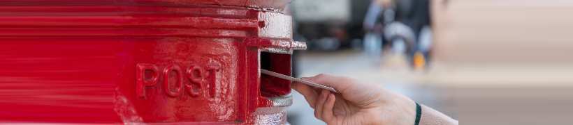 A hand pushing a letter into a postbox.