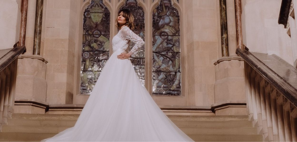 A person in a white wedding dress with a long train stands on a staircase in front of stained glass windows. (Image credit: khays_camera)