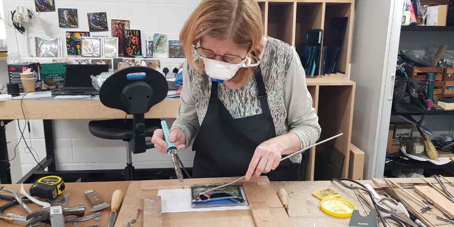 A person painting stained glass in a workshop.