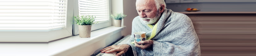 Man wearing blanket sitting next to radiator.