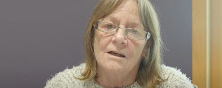A person wearing glasses and a grey jumper.