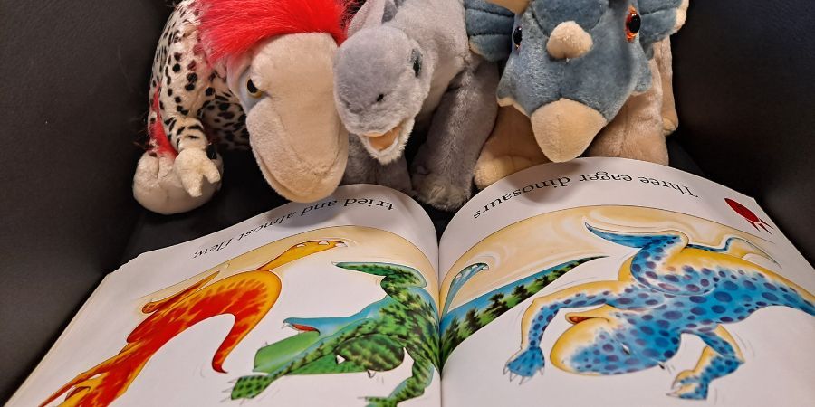 Open children’s picture book on a couch, showing colorful animal illustrations with plush toys resting nearby.