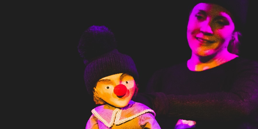 Performer with puppet in dark theatre.