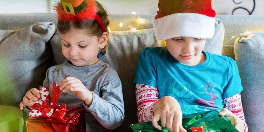 2 children wearing Christmas hats, opening presents.