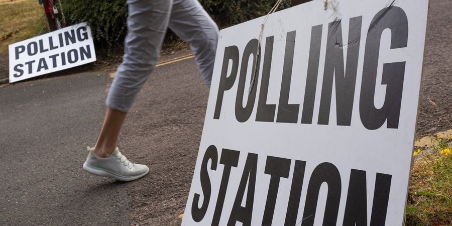 A person walks past a polling station sign on election day. Another polling station sign is visible in the background.