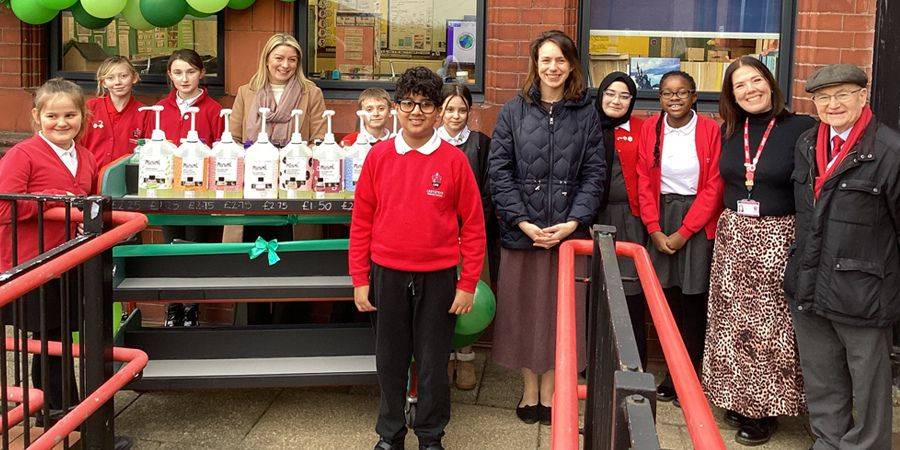 A group of children and adults stand in front of a display of bottles.