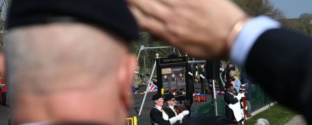 A person in a black beret salutes during an outdoor ceremony with other uniformed individuals in the background.