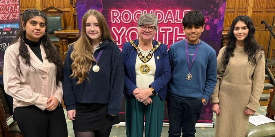 A group of 4 young people and the Mayor stand in front of a banner that reads "Rochdale Youth". The young people are wearing medals around their necks.