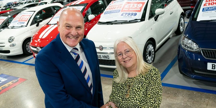 2 people shaking hands in a car showroom.