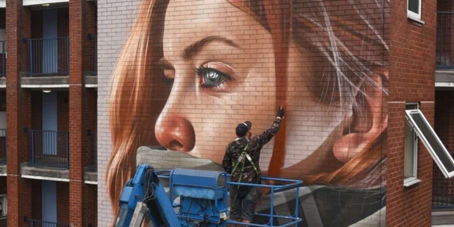 An artist is painting a large mural on the side of a building.