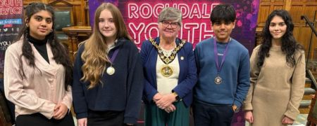 A group of 4 young people and the Mayor stand in front of a banner that reads "Rochdale Youth". The young people are wearing medals around their necks.