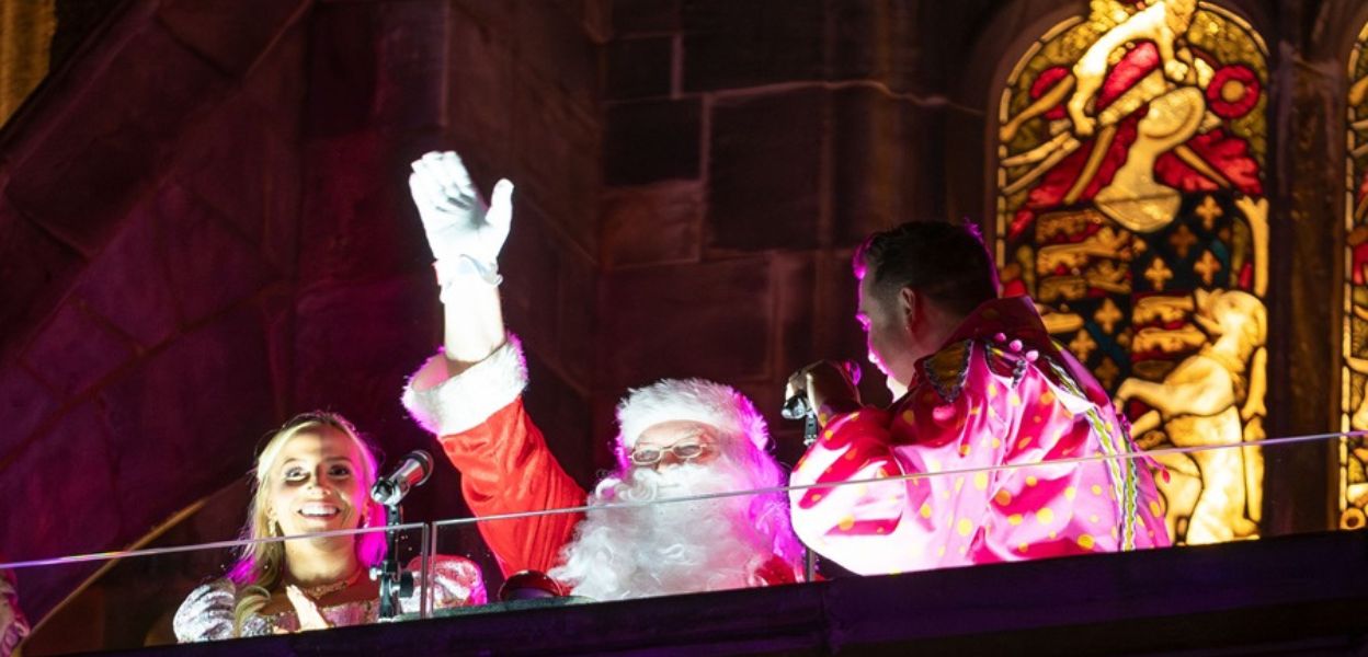 Father Christmas waving while stood in front of a microphone.