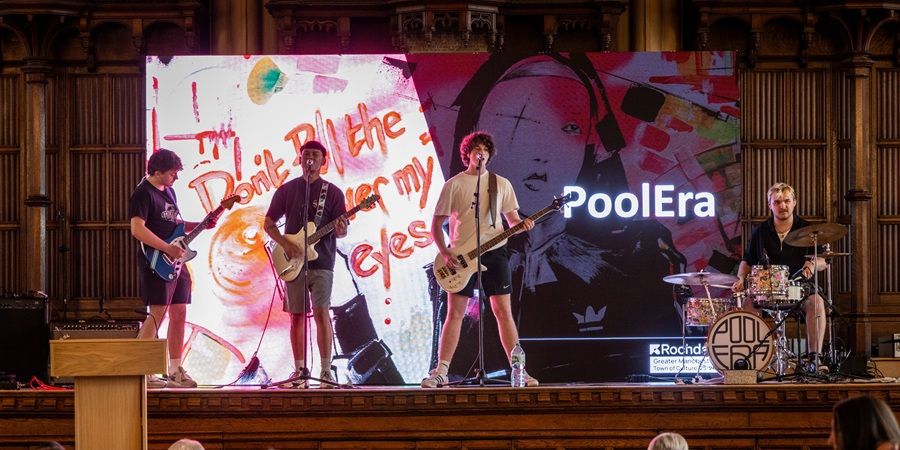 A band on stage in front of a large screen.