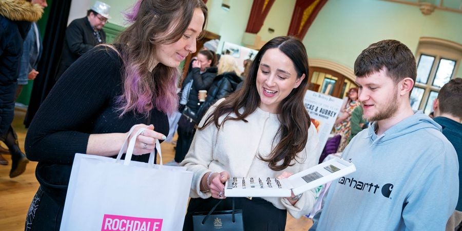 3 people in a busy room looking at a brochure.
