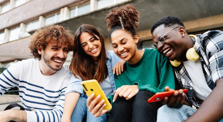 A group of young people smiling looking at a phone.
