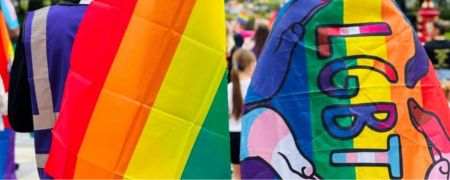 2 people with their backs covered in rainbow coloured flags.