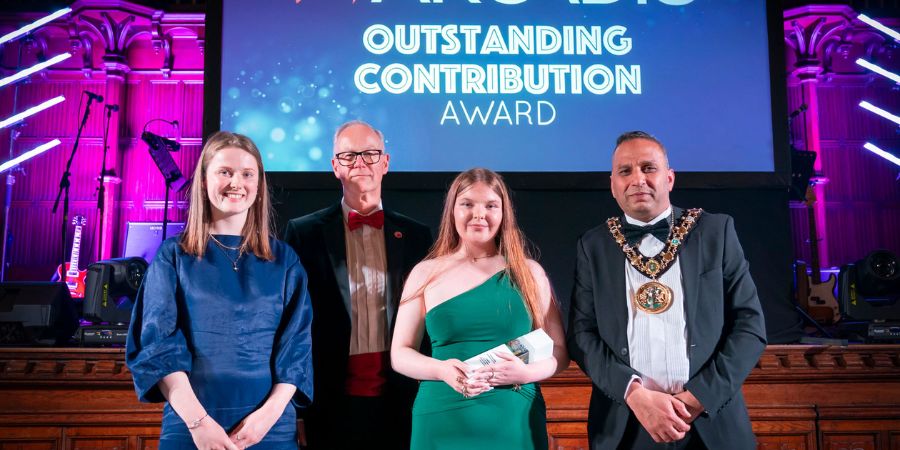 4 individuals stand on stage at an award ceremony, with a backdrop displaying the words "Arcadis Outstanding Contribution Award".