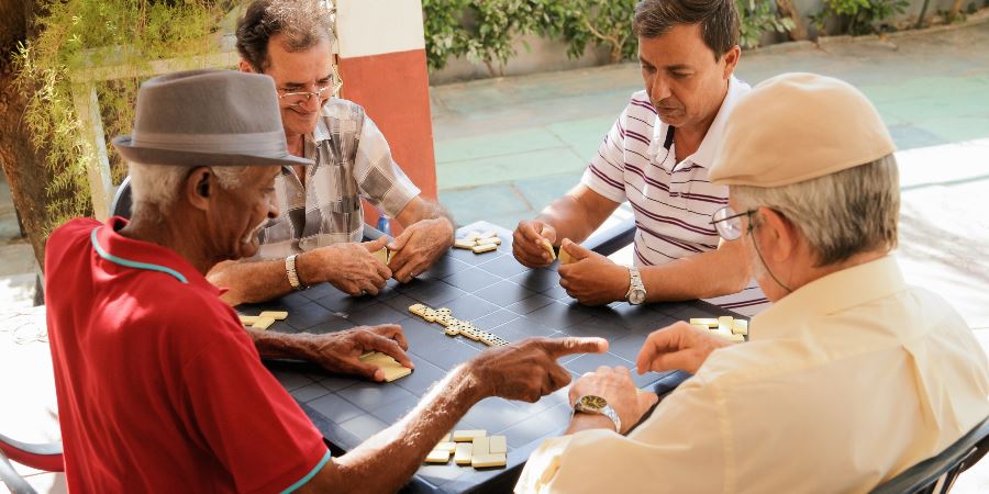 4 men sat at a table playing dominoes.