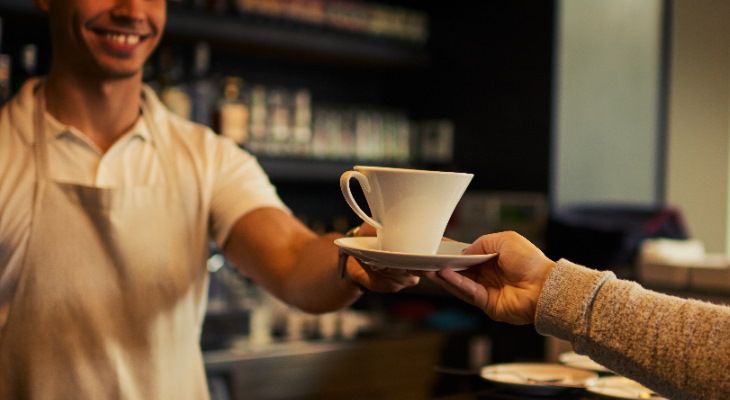 Smiling barista handing a customer a hot drink.
