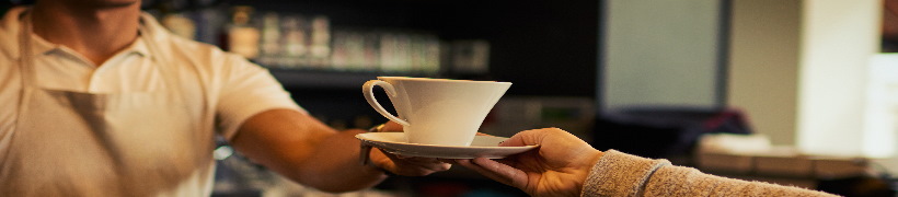 A smiling barista handing a hot drink to a customer.