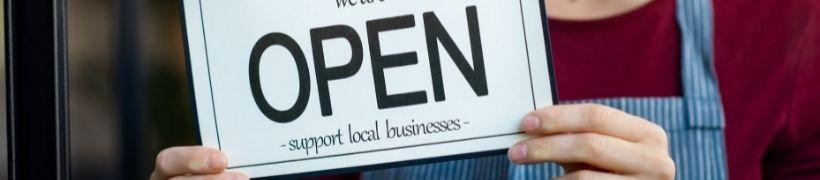 Person holding a sign saying &#039;open - support local businesses&#039;