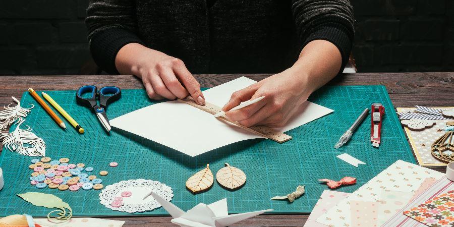 Close-up of hands making a greeting card from materials on the table.