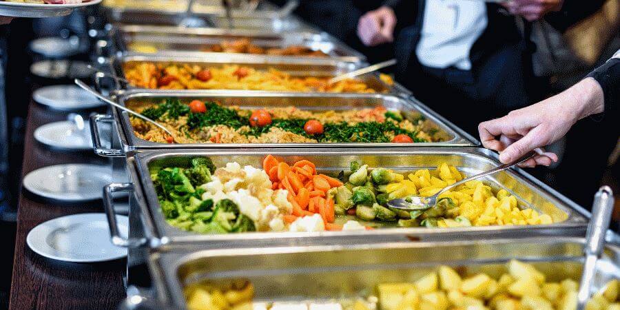 A buffet with food in silver serving trays.