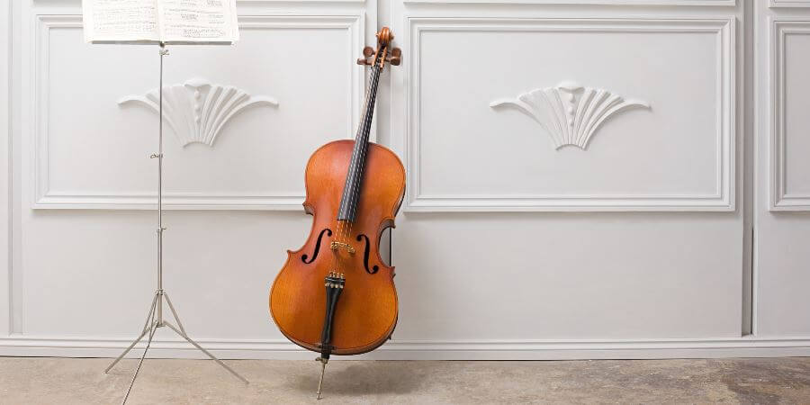 A cello next to a music stand, leaning against a wall.