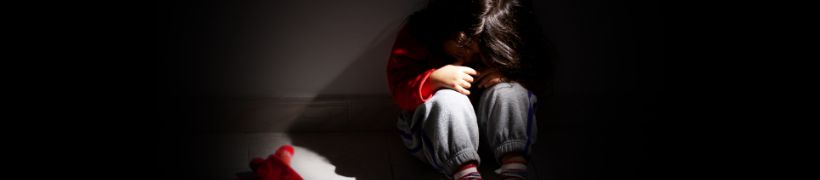 A sad child sitting on the floor alone in the dark.