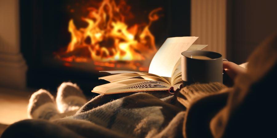 A woman reading with a coffee in front of an open fire.