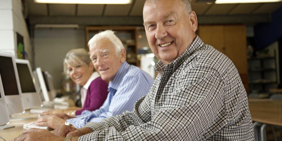 A group of smiling seniors sitting at a bank of computers.