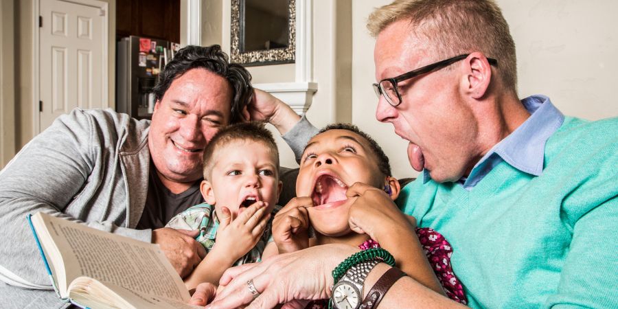 2 boys reading with their 2 fathers, pulling funny faces.