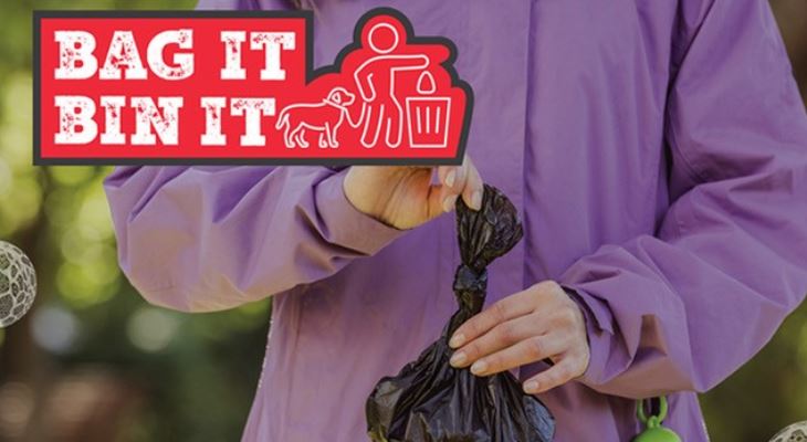 A person holding a black plastic bag, with a Bag It Bin It logo.