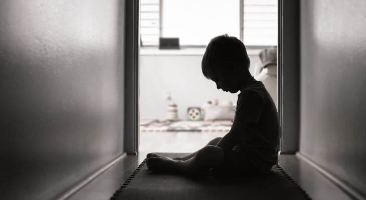 A dejected looking child sitting in a hallway.